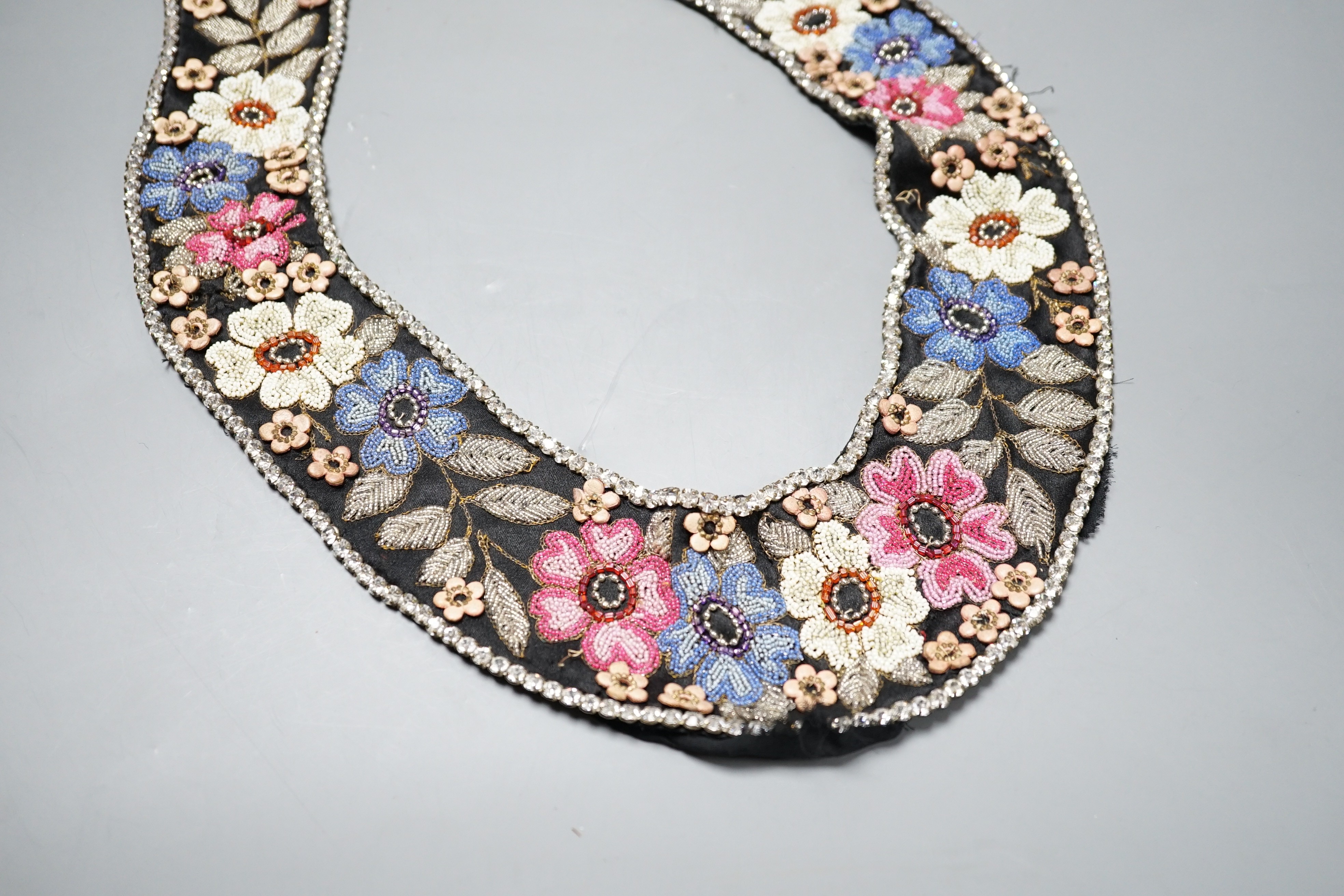 A 1920’s-30’s French beaded collar, the beads embroidered as flowers and leaves with leather applice flowers and diamanté edging, 115 cms long